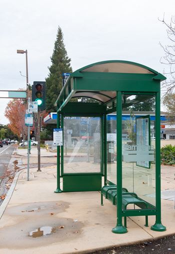 A green bus stop with a bench and a glass window.